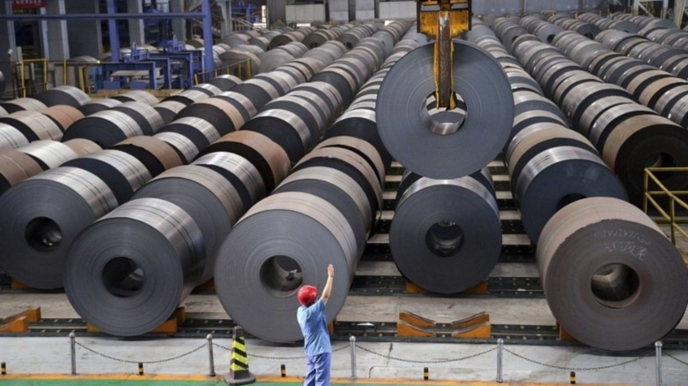 A worker standing in front of rolls of steel at a manufacturing plant. Blog Image